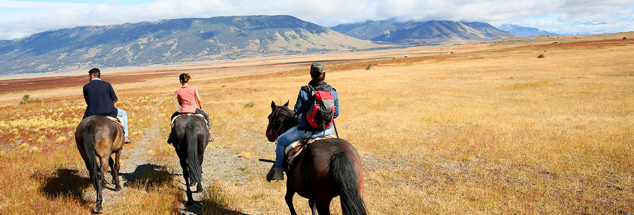 three people riding on horseback through plains with the mountains in the background