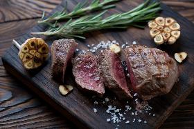 a piece of rare steak prepared on a wooden board with lotus seeds and greens 